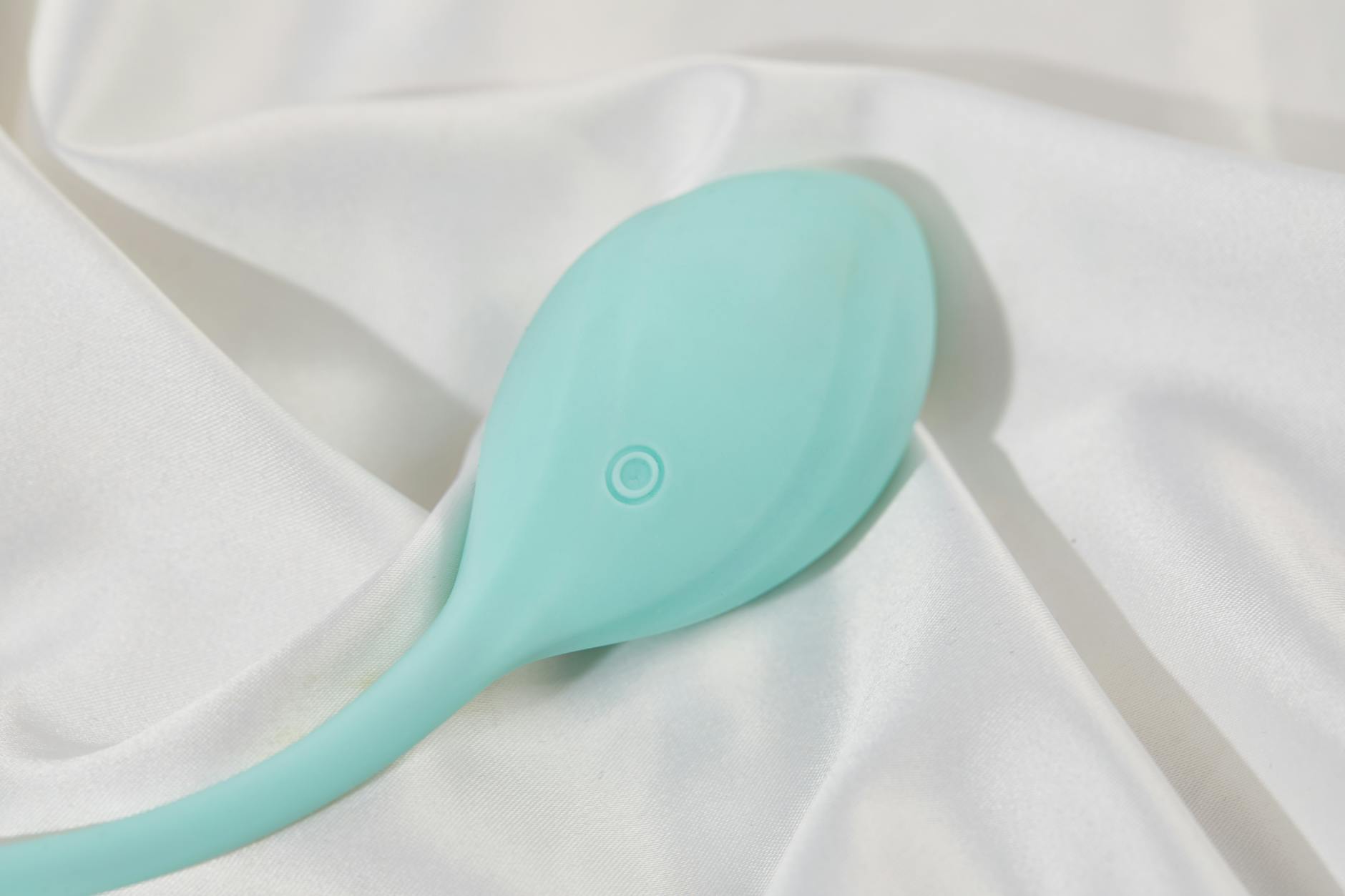 A stylish teal vibrator on smooth white silk fabric, representing intimacy and self-care.