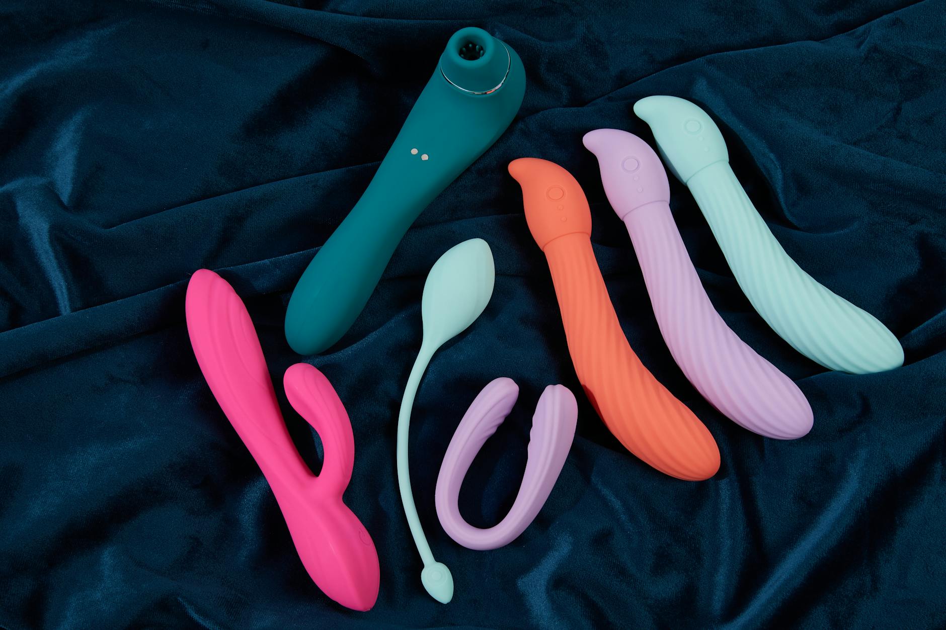 Vibrant display of silicone sex toys on dark blue fabric, showcasing various colors and shapes including lemon vibrators.