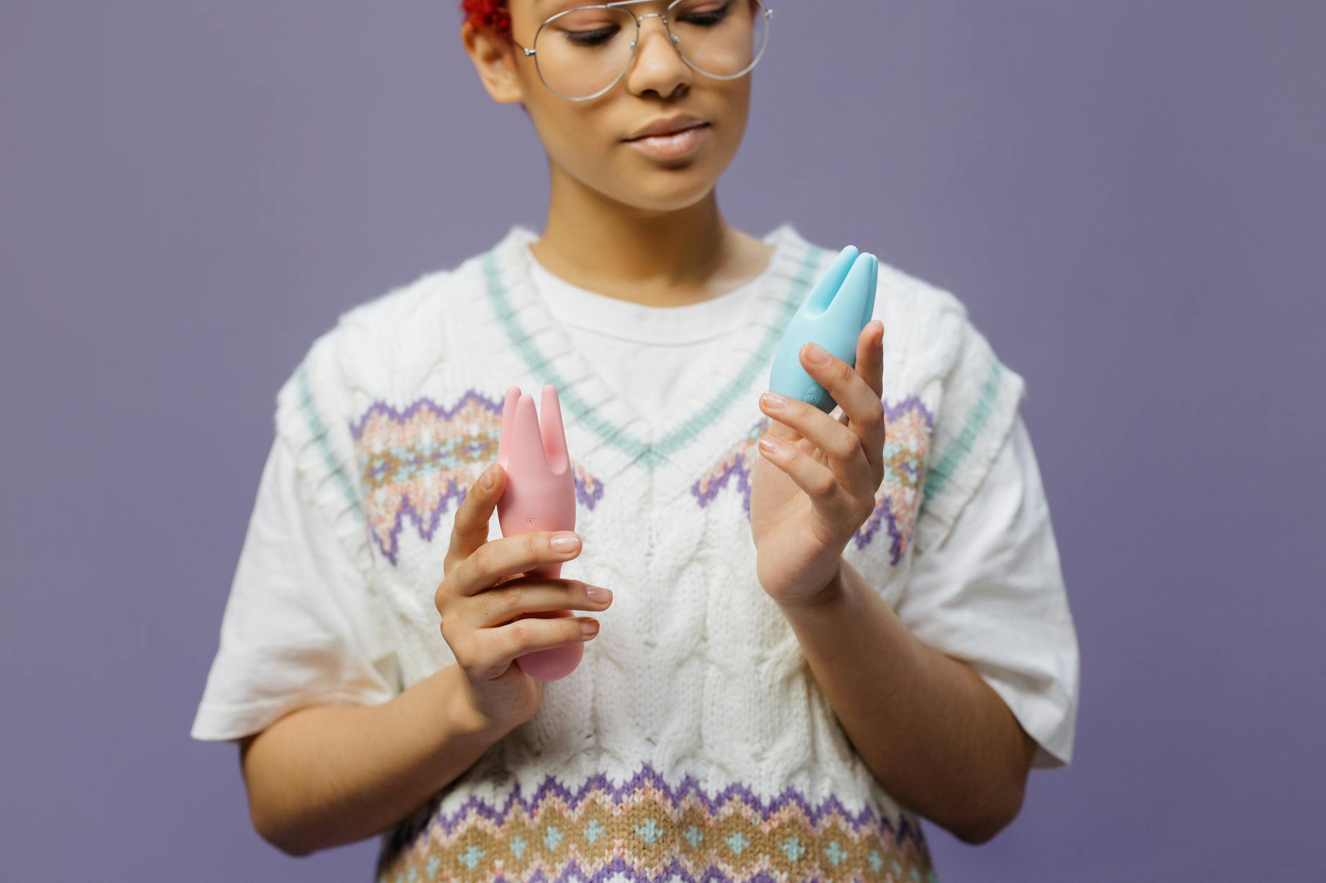 Woman holding blue and pink silicone vibrators, exploring clitoral pleasure and self-connection.