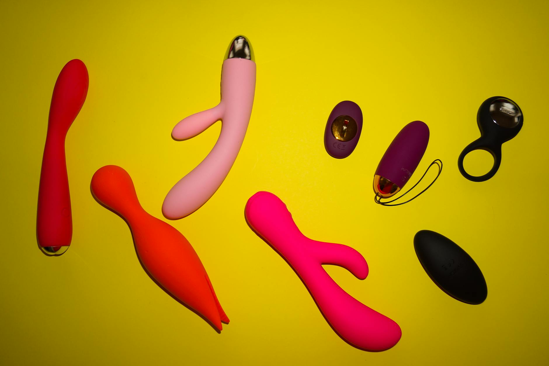 Two hands holding pink and blue silicone vibrators against a pastel background.